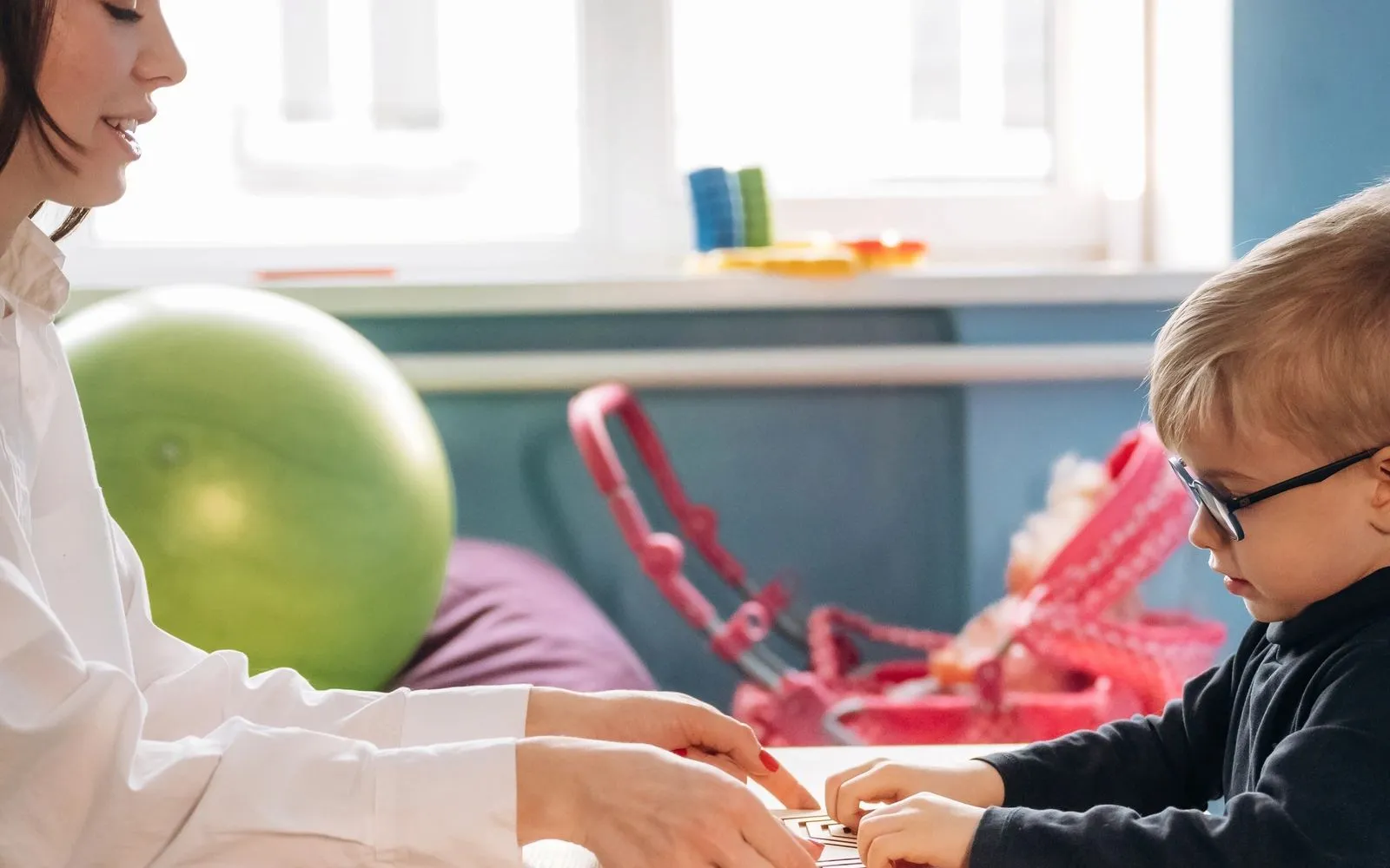 A preschool child exploring a book with an educator nearby